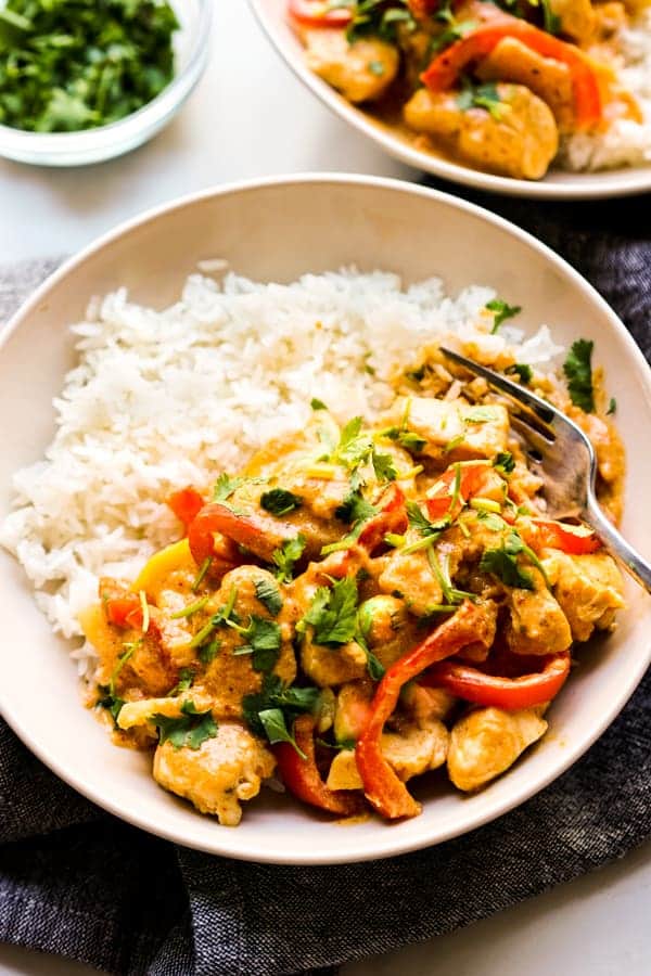 Close up of a bowl of rice topped with Thai curry with chicken, bell peppers and zucchini.