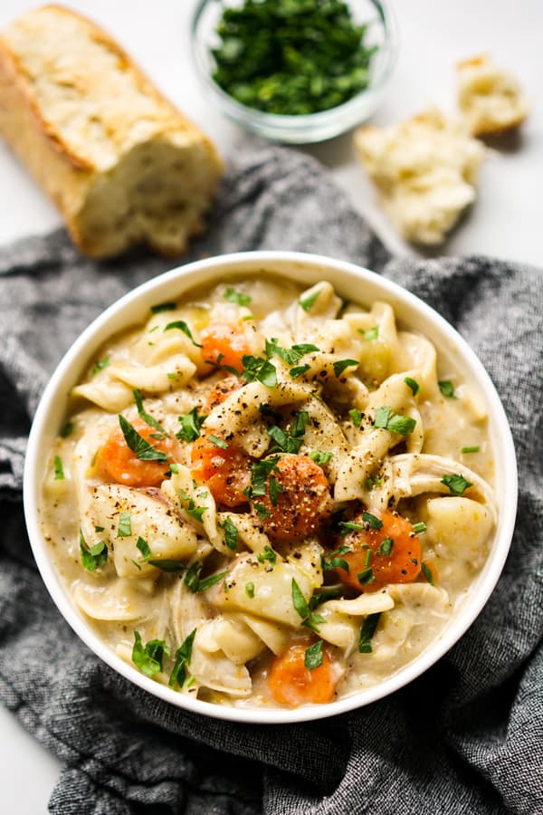 A close up of a bowl of Instant Pot Creamy Chicken Noodle Soup with bread in the background