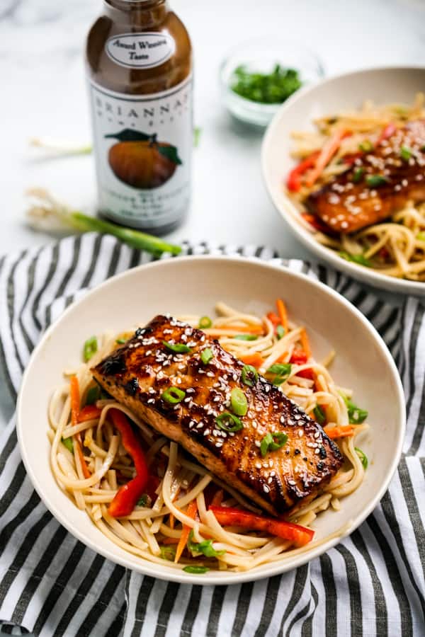 A bowl of noodles with salmon on top, with a BRIANNAS dressing in the background