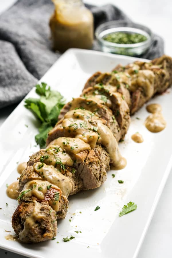 Slices of pork tenderloins on a plate, topped with cream sauce and parsley