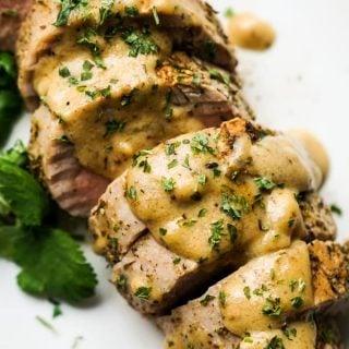 Close up of roasted pork tenderloins topped with gravy and chopped parsley