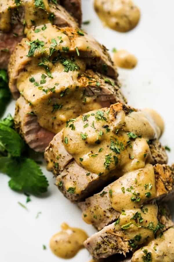 Close up of roasted pork tenderloins topped with gravy and chopped parsley