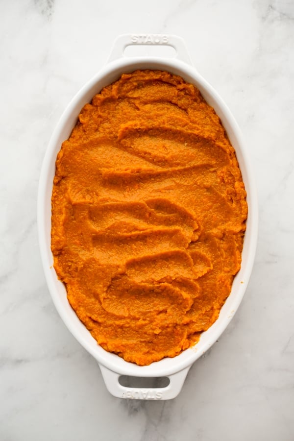 A rectangular casserole dish filled with mashed sweet potatoes, and a round bowl filled with pecan crumbles