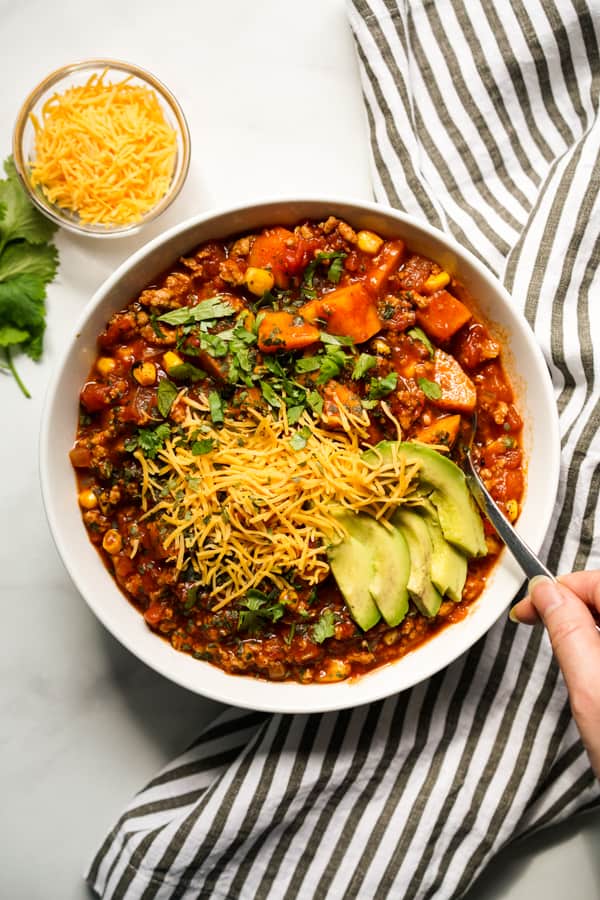 Top down view of a bowl of chili filled with sweet potatoes, turkey, avocados, cilantro and cheese