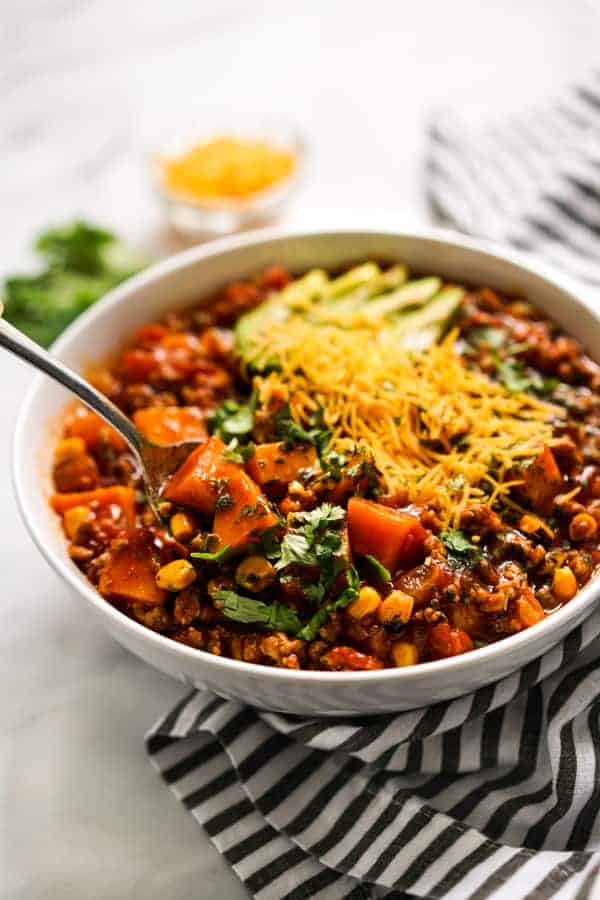 Spoon digging into a bowl of Turkey Sweet Potato Chili with garnishes