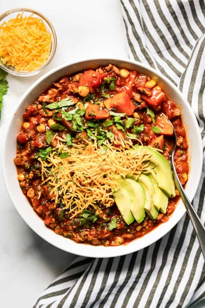 Top down view of a bowl of chili topped with sliced avocados, cheese and cilantro