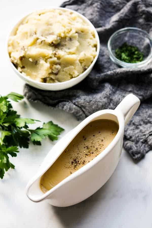 Gravy boat filled with homemade gravy with mashed potatoes and fresh parsley in the background