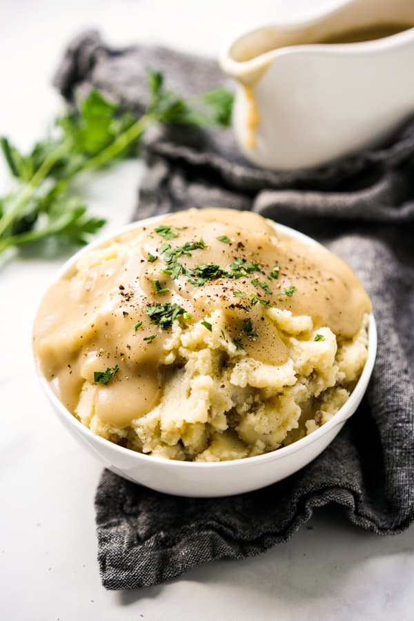 A bowl of potatoes with brown gravy on top