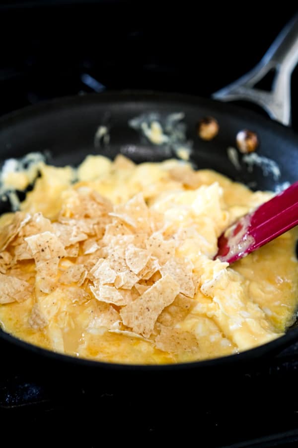 Adding tortilla chips to scrambled eggs in a skillet