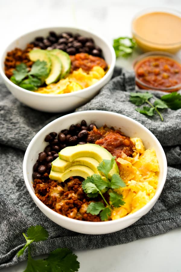 Two bowls of scrambled eggs, chorizo, salsa, black beans and avocado