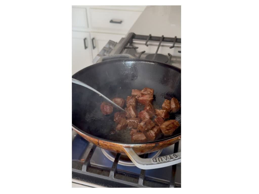 Searing steak pieces in a large wok under high heat