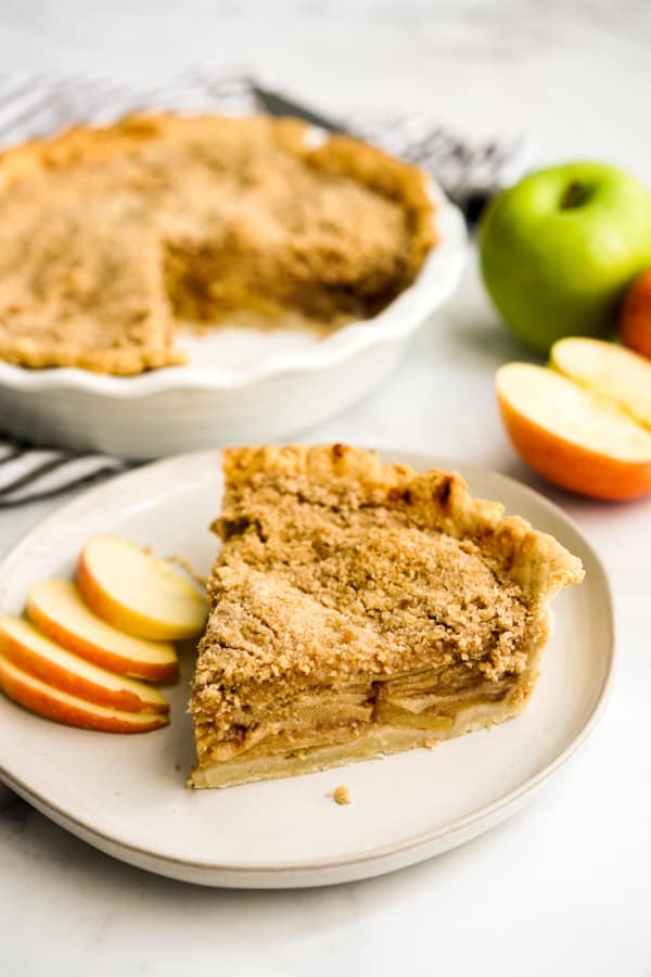 A slice of pie topped with vanilla ice cream with a whole pie in the background