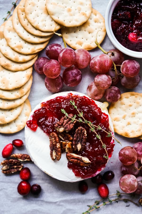 Top down view of Baked brie topped with cranberry sauce, surrounded by crackers and grapes