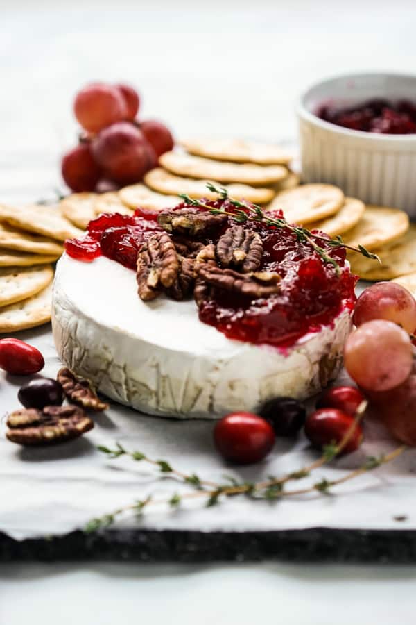 Cranberry Baked Brie with crackers and a small bowl of cranberry sauce and crackers in the background