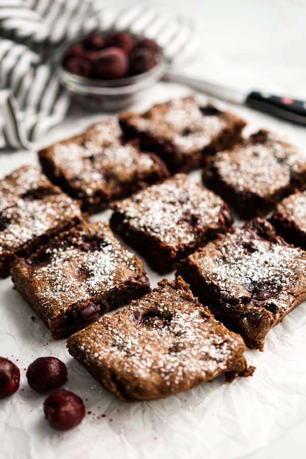 9 square Chocolate Cherry Brownies topped with powdered sugar, a bowl of cherries in the background