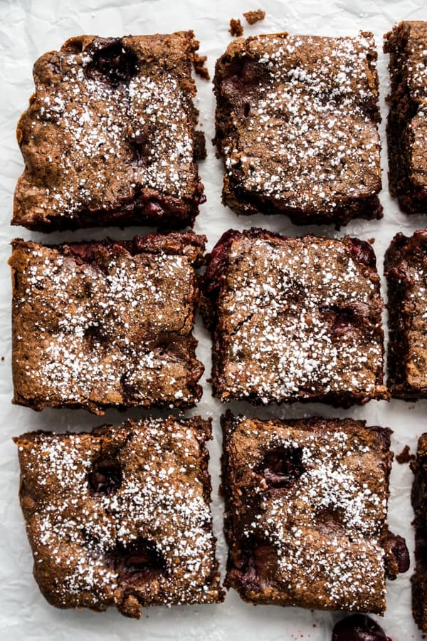 Six square pieces of chocolate brownies loaded with cherries, topped with powdered sugar