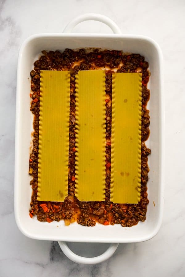 Lasagna noodles on top of bolognese sauce in casserole dish