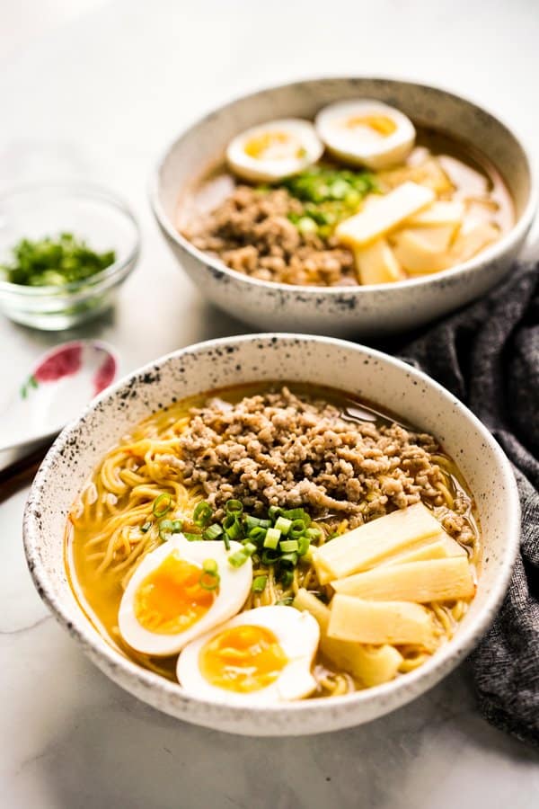Two bowls of ramen noodles with boiled eggs, bamboo shoots and pork.