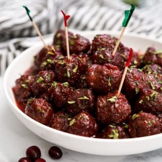 A bowl of meatballs with sticky sauce and toothpicks on a few of them