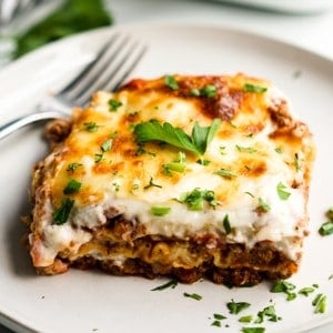 A slice of lasagna layered with with bachemel sauce and bolognese meat sauce on a plate with a fork in the background