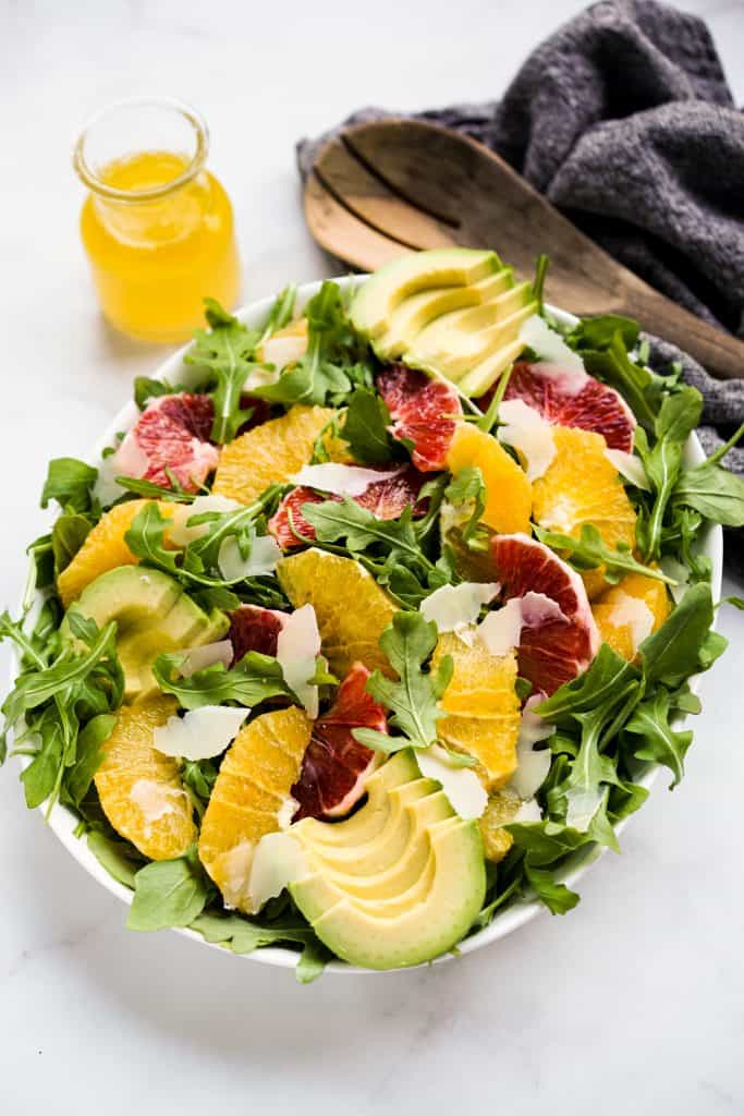 A bowl of arugula salad with avocados, oranges, blood oranges and parmesan on top