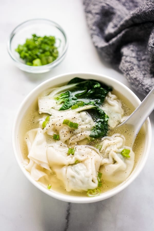 A bowl of wonton soup with spoon in it