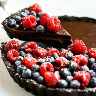 Cutting out a slice of chocolate tart topped with blueberries and raspberries