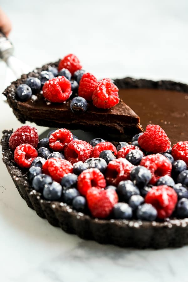 Cutting out a slice of chocolate tart topped with blueberries and raspberries