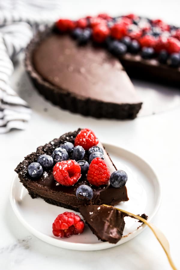 A slice of chocolate tart topped with berries on a plate being cut into with a fork