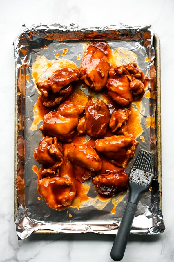 Chicken thighs on a baking sheet lined with aluminum foil brushed with sauce