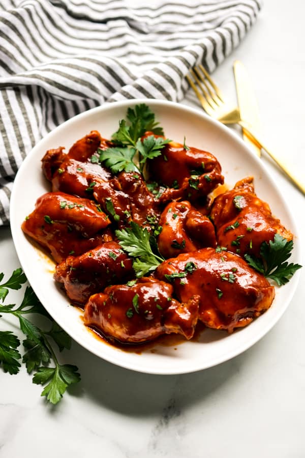 An oval plate of chicken thighs covered in sticky bbq sauce