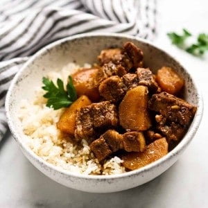 A bowl of pork belly and potatoes in soy sauce on top of rice