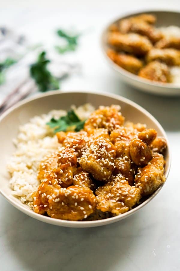 A bowl of rice topped with sticky honey sesame chicken 