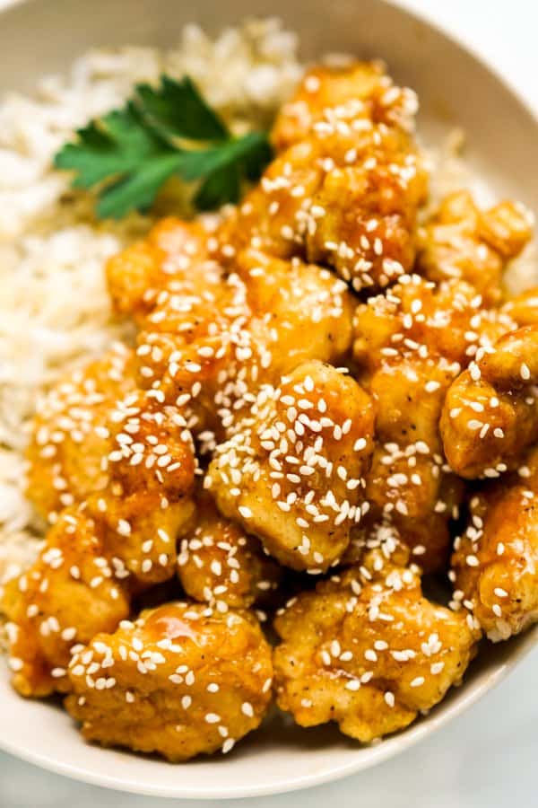 closeup of breaded crispy chicken coated in sesame sauce sprinkled with sesame seeds