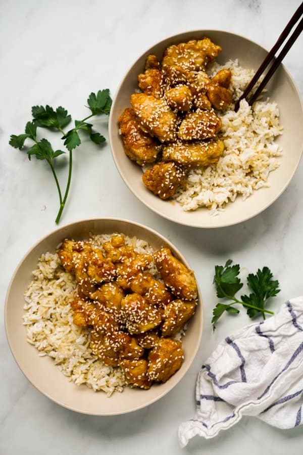 Top down shot of two bowls of crispy chicken coated in sesame sauce on rice