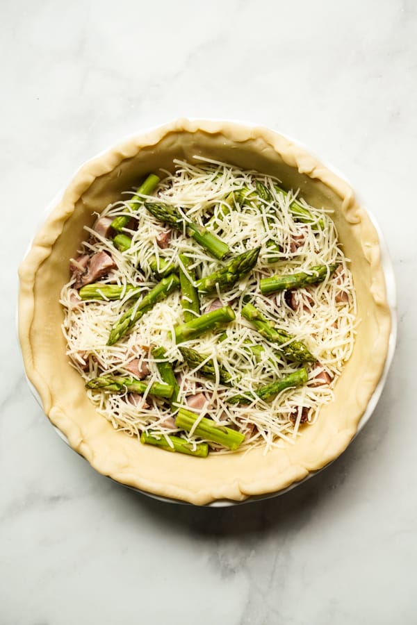 Unbaked pie crust topped with asparagus, ham and cheese