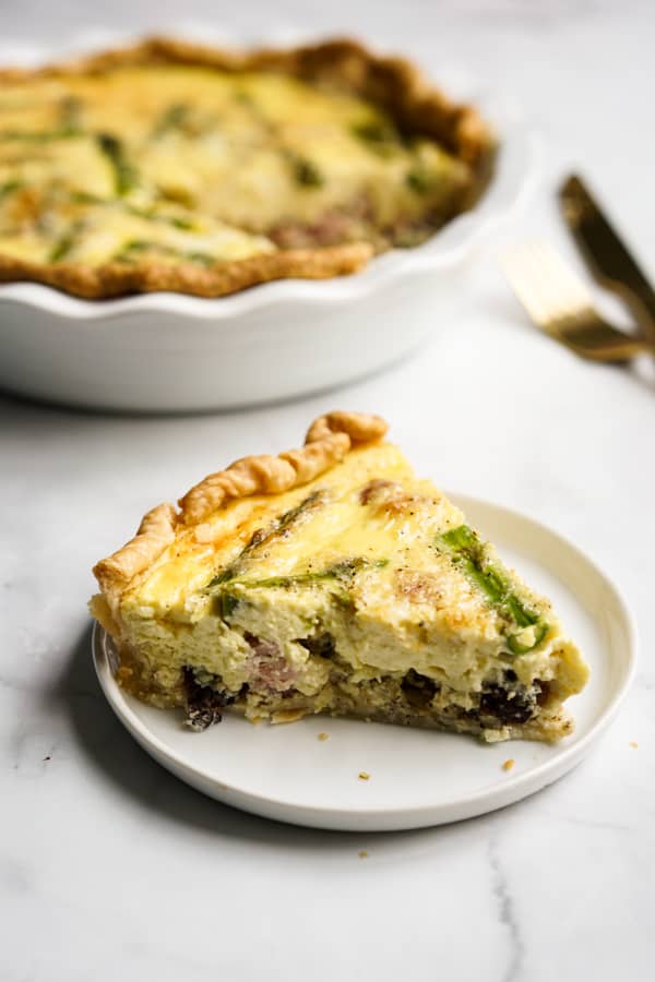 A slice of quiche on the plate with the whole quiche in the background