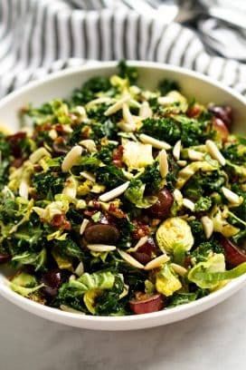 A bowl of Kale and Brussels Sprouts Salad topped with almonds and bacon vinaigrette