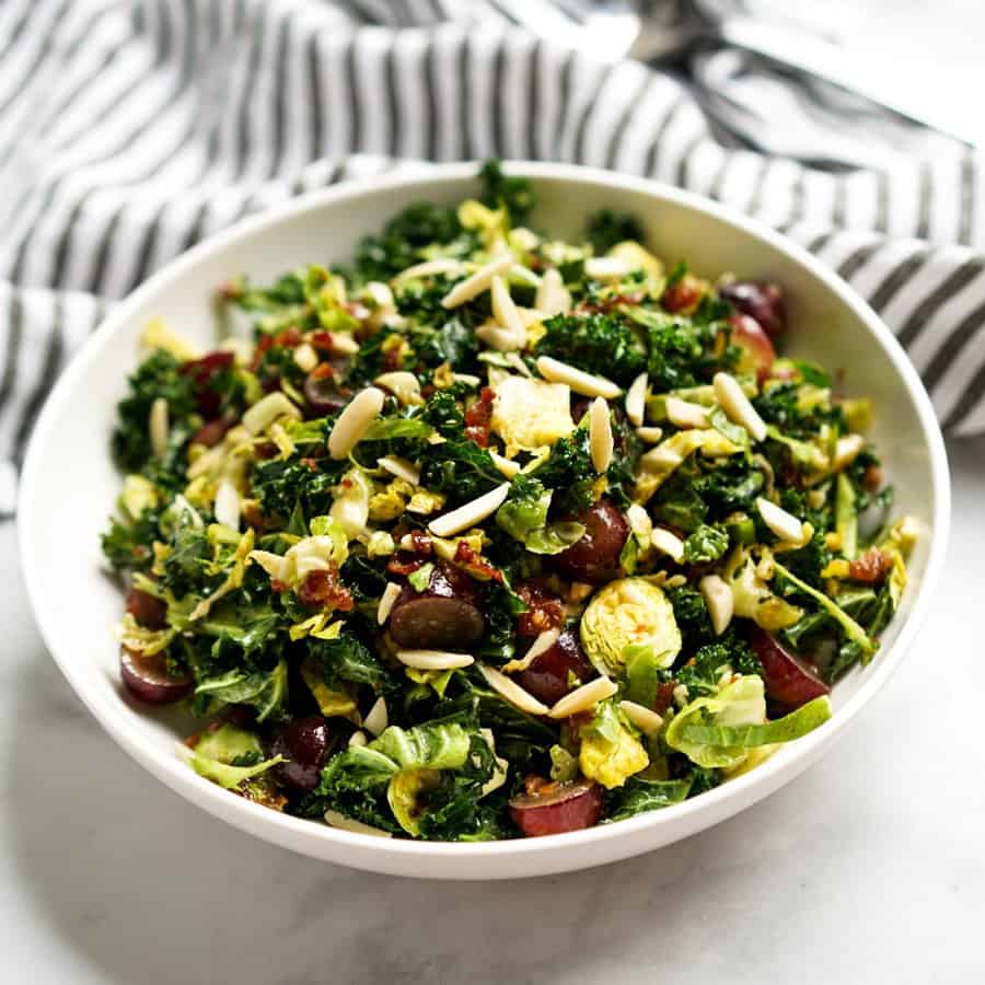 A bowl of Kale and Brussels Sprouts Salad topped with almonds and bacon vinaigrette