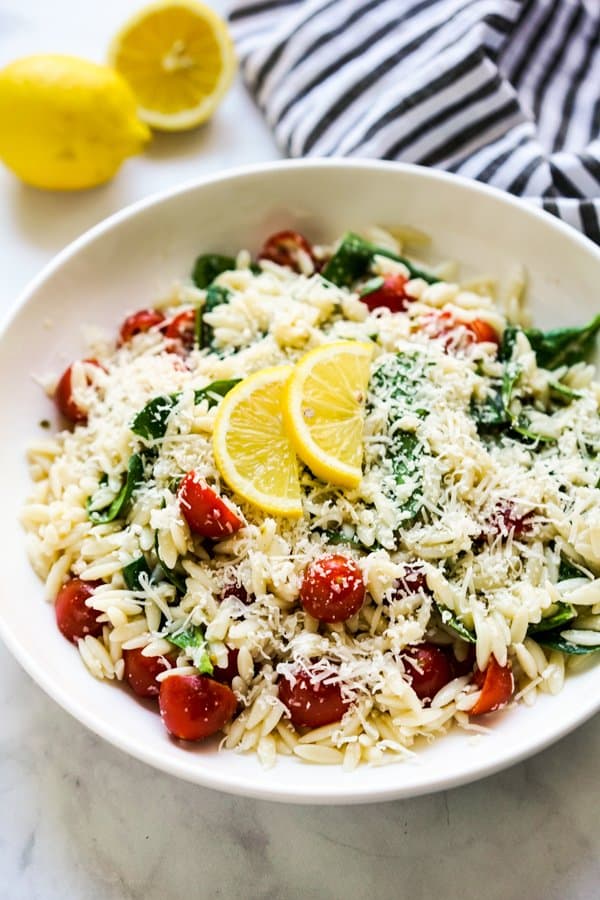 A bowl of lemony orzo pasta topped with parmesan and lemon slices