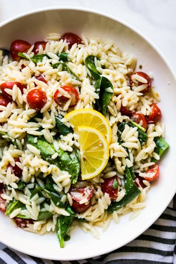 Close up of orzo pasta tossed with spinach and cherry tomatoes, garnish with sliced lemons 