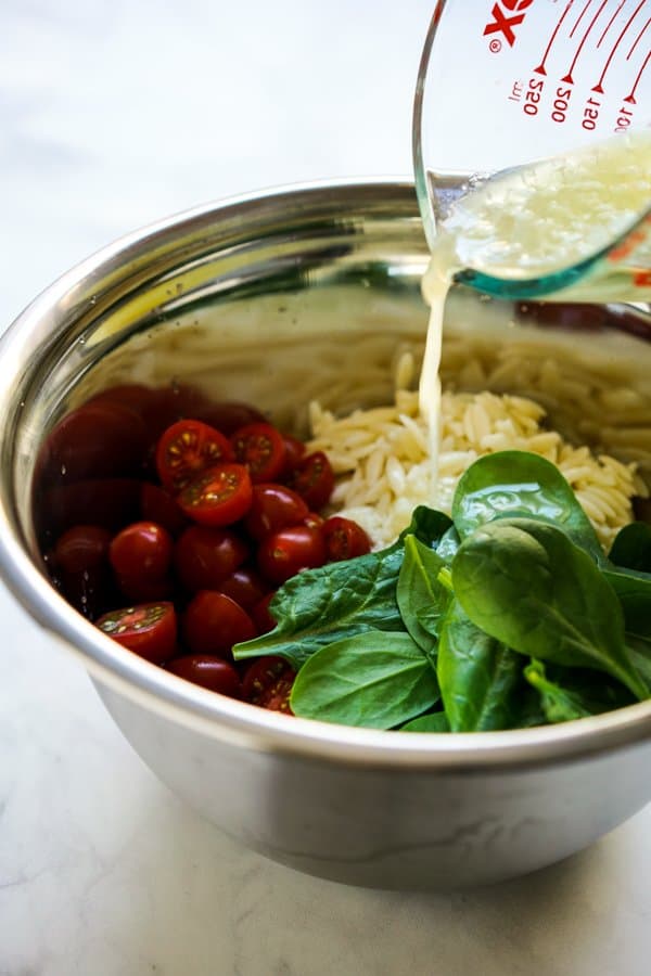 Adding lemon juice to a bowl of spinach, cherry tomatoes and orzo 