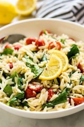 A bowl of orzo tossed with spinach, tomatoes, with lemon wedges on top