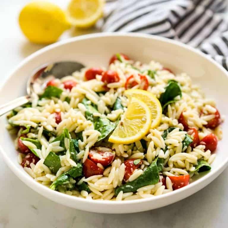 A bowl of orzo tossed with spinach, tomatoes, with lemon wedges on top