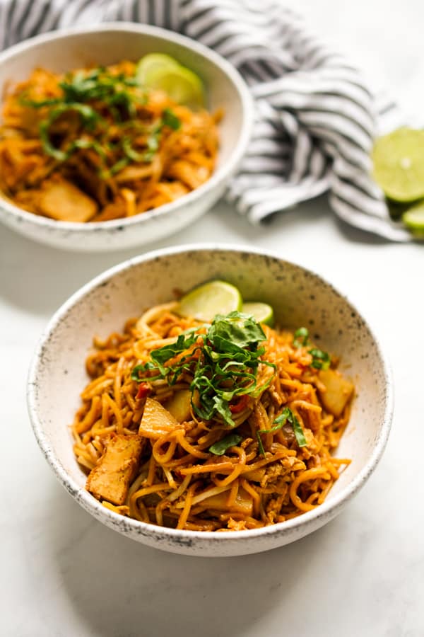 Two bowls of Mee Goreng Mamak style garnished with lettuce and lime wedges