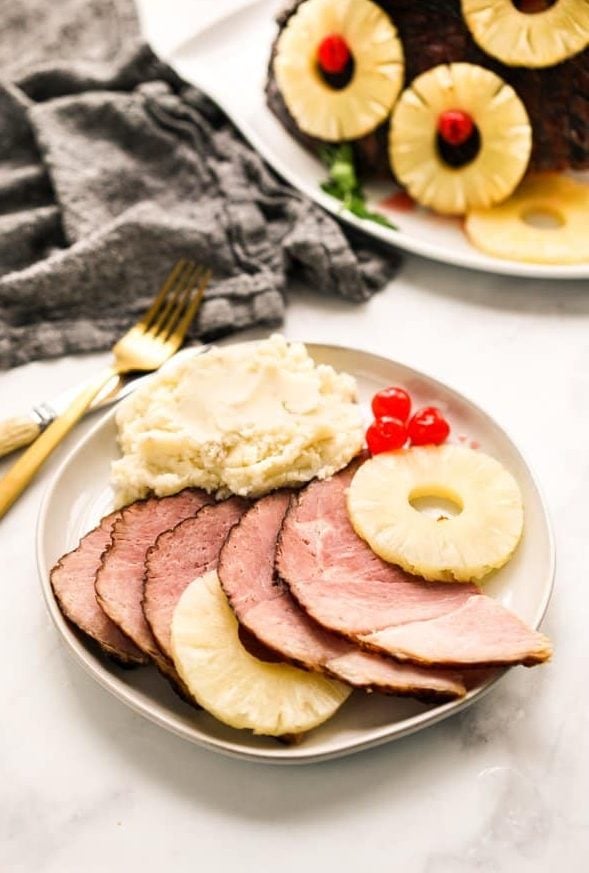 A plate of sliced ham with pineapple rings and mashed potatoes