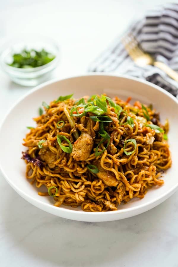 a plate of Tom Yum Fried Noodles topped with chicken and green onions