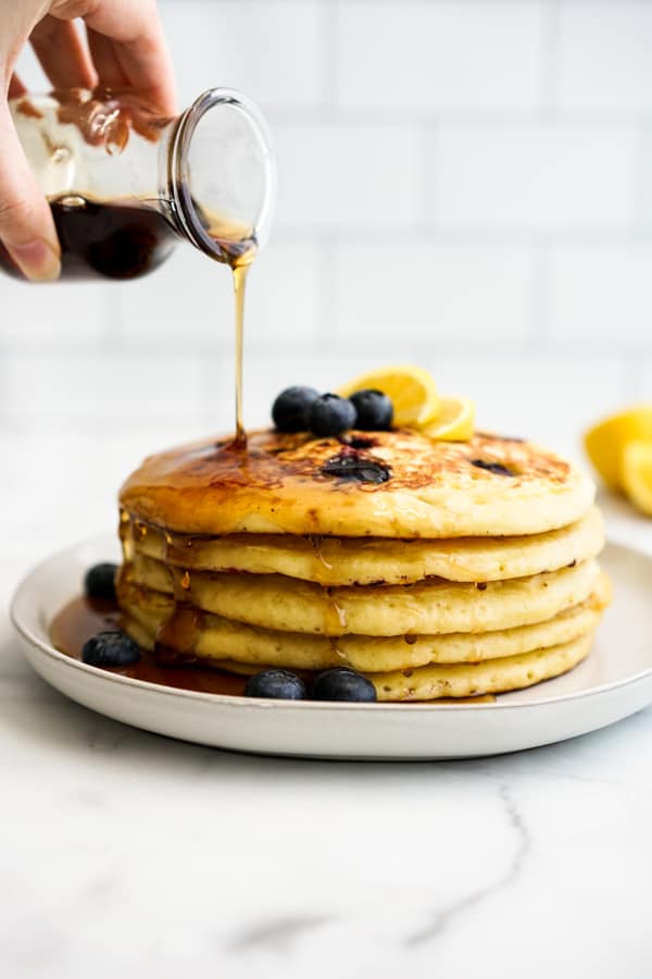 Drizzling syrup over a stack of lemon blueberry pancakes
