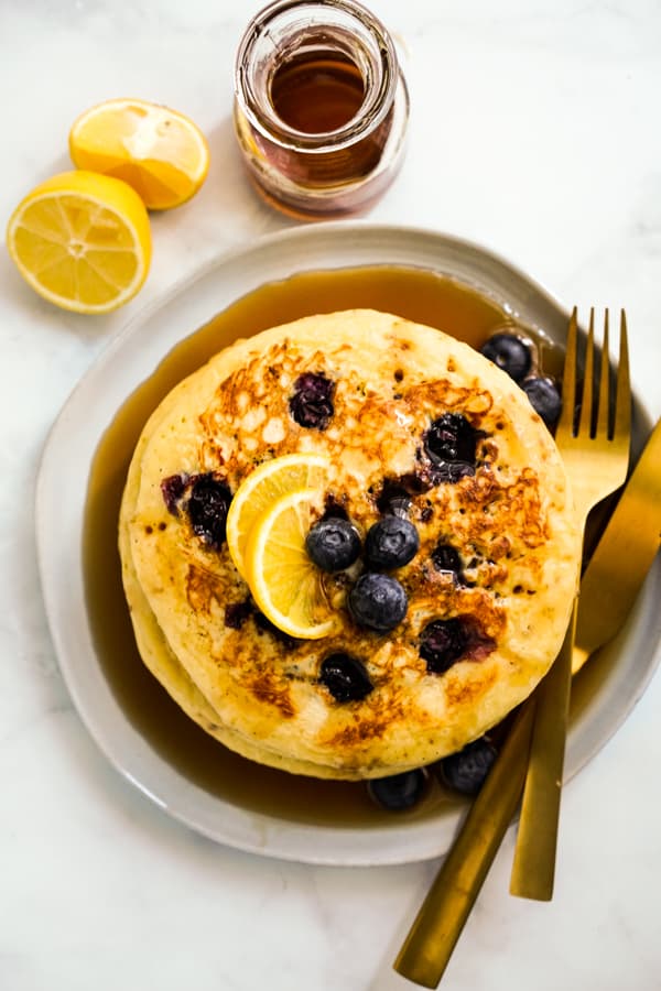 A plate of of stack of pancakes with lemons and blueberries, fork and knife on the side