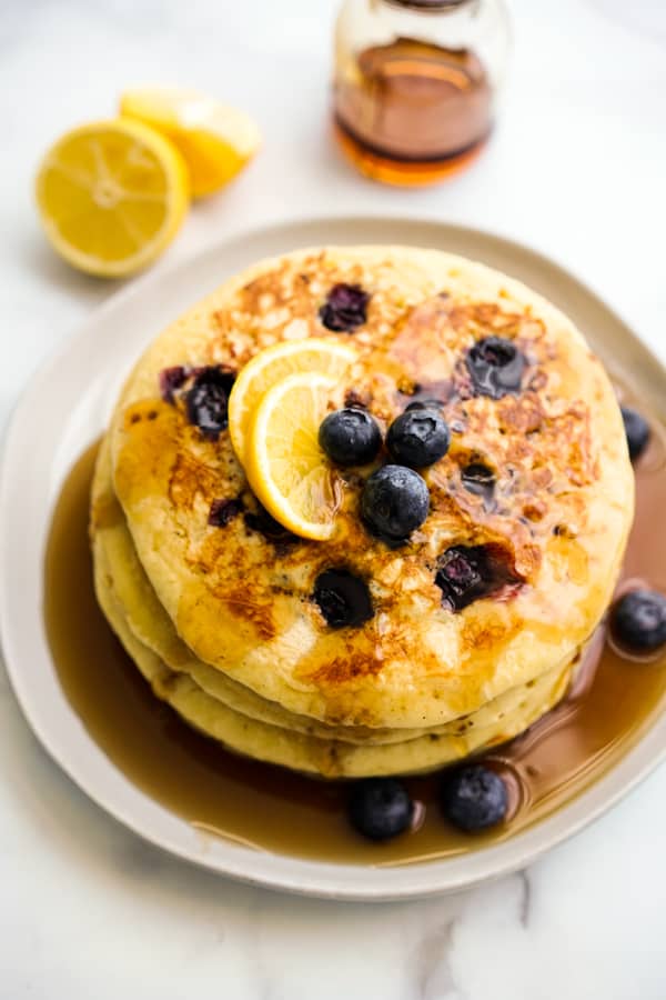 A stack of pancakes in maple syrup, along with blueberries and lemon slices